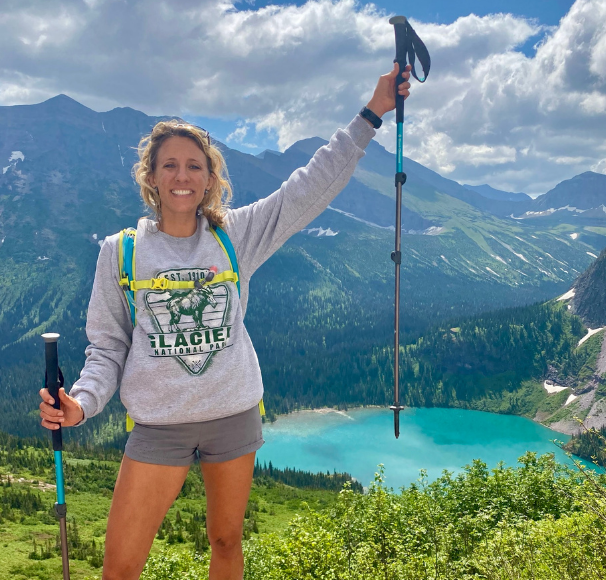 Woman with hiking gear in front of a lake and mountain range