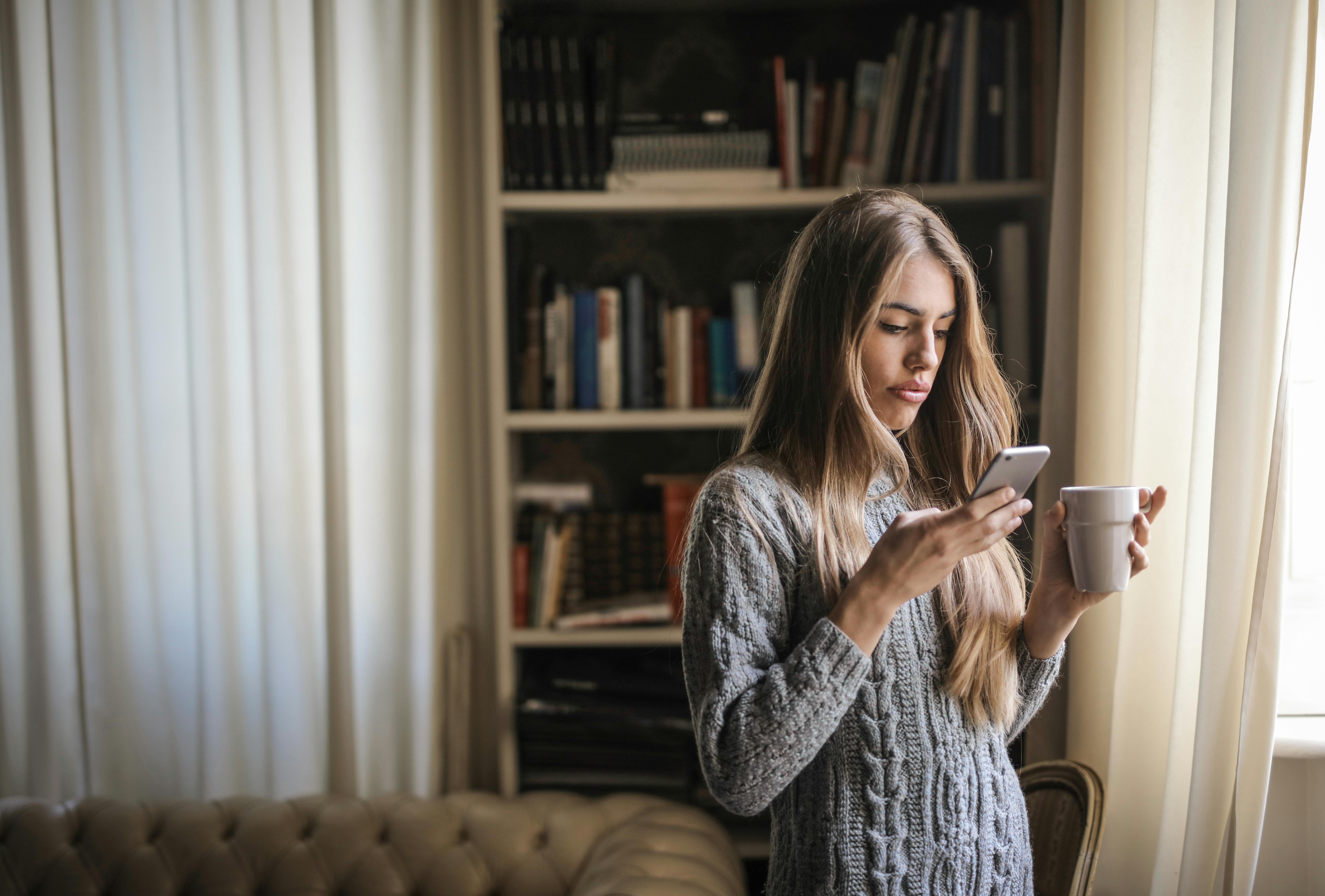 travel therapist texting recruiter with cup of coffee in hand