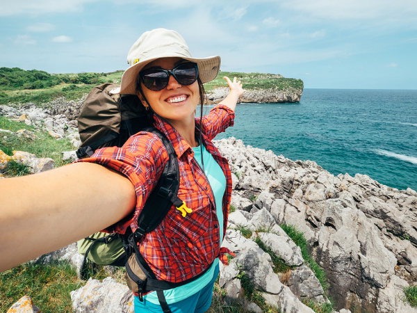 Woman taking a selfie by the coast while wearing a backpack